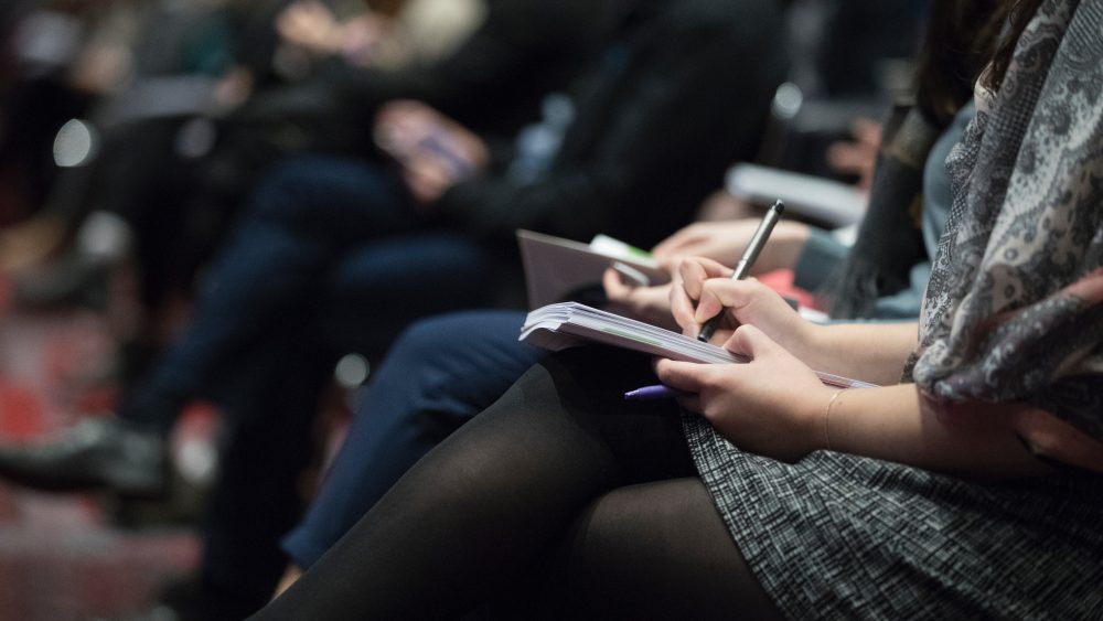 Attendees take notes at a conference.
