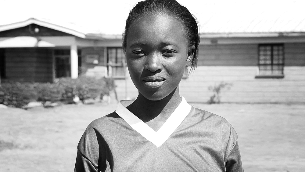 A young woman stands outside her school in Kenya.